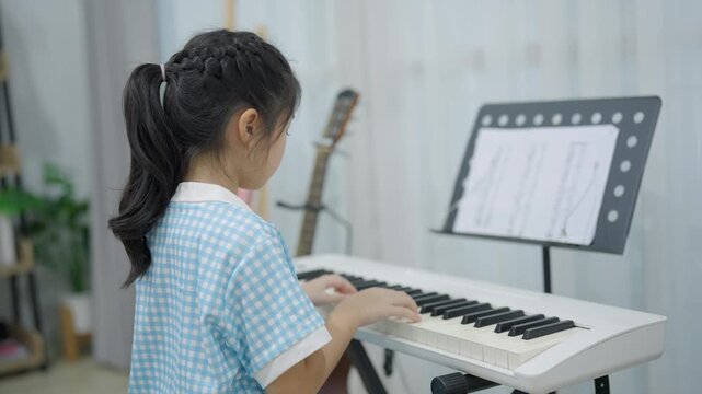 Young girl practicing keyboard piano at home with focused posture and music sheet on stand in cozy room setting