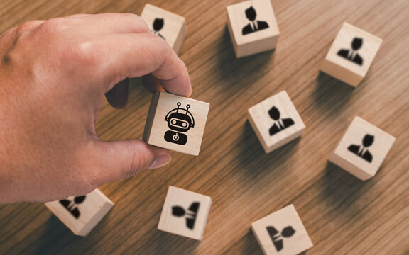 Hand choosing wooden block with robot icon among people icons on wooden background. Artificial intelligence replacing human workforce, automation, technology, and recruitment business concept