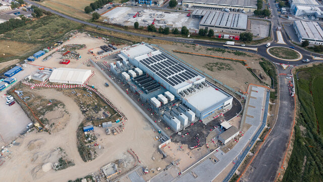 Aerial view of the BYES MIL08 data center facility with rooftop solar panels and industrial cooling units, located in an industrial area near a roundabout in Siziano, Lombardia, Italy.