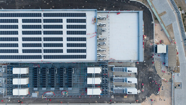 Aerial view of a large industrial facility featuring extensive rooftop solar panel arrays and ground-level cooling units in Siziano, Lombardia, Italy.
