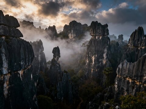 Mist-covered limestone karsts rise dramatically against a cloudy sky in a rugged mountain landscape.