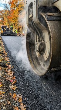 Heavy Machinery Compacting Hot Bitumen on a Scenic Autumn Roadway Construction Site