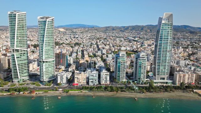 Aerial view of Limassol skyline and waterfront. Tall buildings, coastal road, beach and blue sea create a modern urban travel landscape.