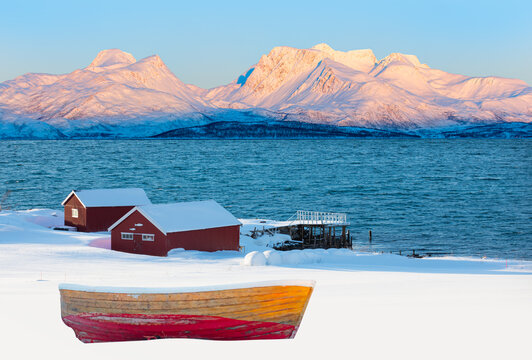 Fisher shelter in winter with fishboat at sunset in the background snowy mountains and Norwegian fjords - Tromso, Norway