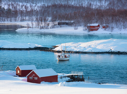 Fisher shelter in winter with fishboat at sunset in the background snowy mountains and Norwegian fjords - Tromso, Norway