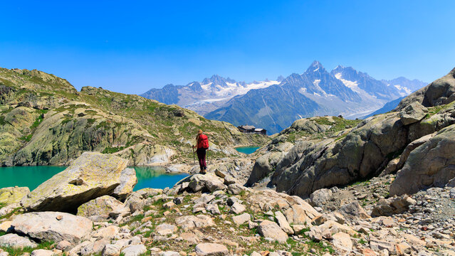 Rear view of female hiker with red backpack standing on rock looking at alpine lake and mountain peaks, Lac Blanc near Chamonix