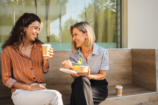 Two businesswomen sitting outside, talking and having lunch together