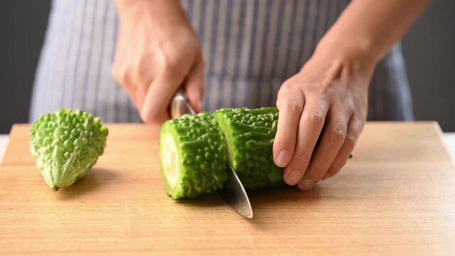 Woman hands holding a kitchen knife and chopping bitter gourd on a wooden cutting board