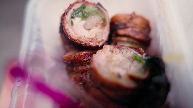 Smoky charred meat rolls stuffed with herbs rest in a takeaway container at a Sicilian street food stall, close up.