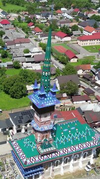 Aerial drone footage circling the colorful church and vibrant painted wooden crosses of the Merry Cemetery (Cimitirul Vesel) in Sapanta, Romania.