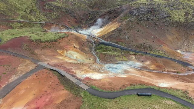 Aerial perspective of the Seltun Geothermal Area in Iceland. Colorful mineral deposits, steaming fumaroles, and people walking on pathways