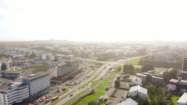Aerial drone shot shows a person ziplining across a busy road with traffic in the city of Reykjavik, Iceland. The bright, hazy cityscape spreads out in the background.