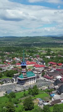 Aerial drone footage flying toward the colorful church and painted wooden crosses of the Merry Cemetery (Cimitirul Vesel) in Sapanta, Romania.