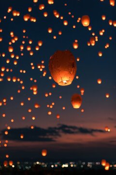 Numerous glowing orange sky lanterns float upward during a nighttime festival