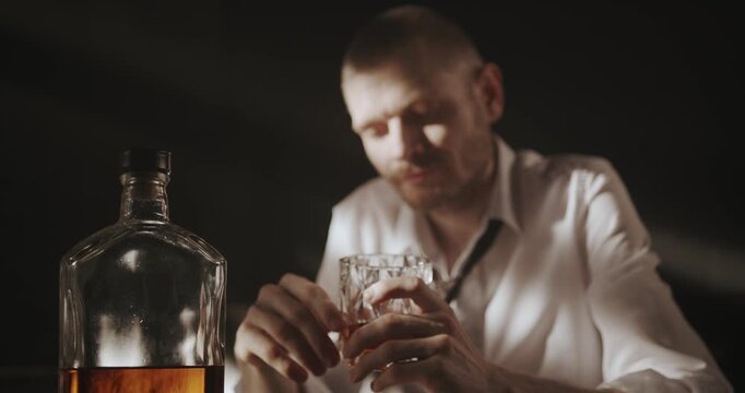 Man stares at a glass of liquor before rejecting the drink and covering his face in emotional distress.