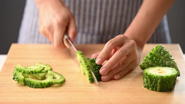 Woman hands holding a kitchen knife and slicing bitter gourd on a wooden cutting board