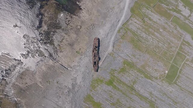 Rusting Plassey shipwreck sits on a bare rock shore between Atlantic surf and patterned stone fields as the camera moves overhead.