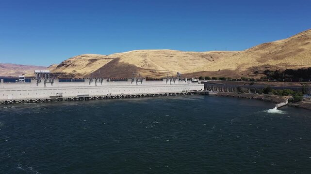 4K aerial drone footage of John Day Dam near Rufus, Oregon, USA with distant wind turbines. Hydroelectric power station, renewable energy, pelicans fishing in Columbia River Gorge
