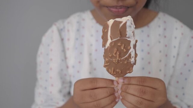 a child enjoys a chocolate ice cream bar while holding it close