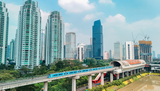 Aerial view of the MRT Jakarta train traveling on an elevated track through the modern skyline with glass skyscrapers, lush trees, and urban infrastructure in Jakarta, Indonesia.