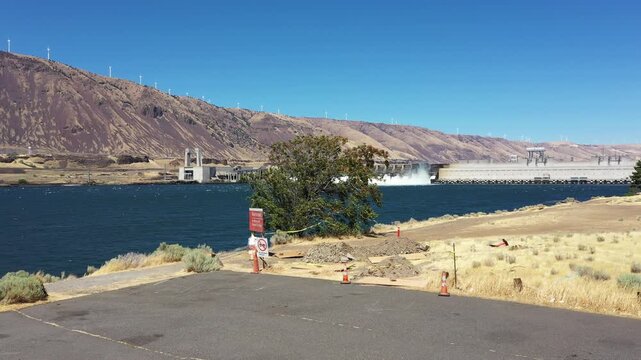 4K aerial drone footage of John Day Dam near Rufus, Oregon, USA with distant wind turbines. Hydroelectric power station, renewable energy, pelicans fishing in Columbia River Gorge