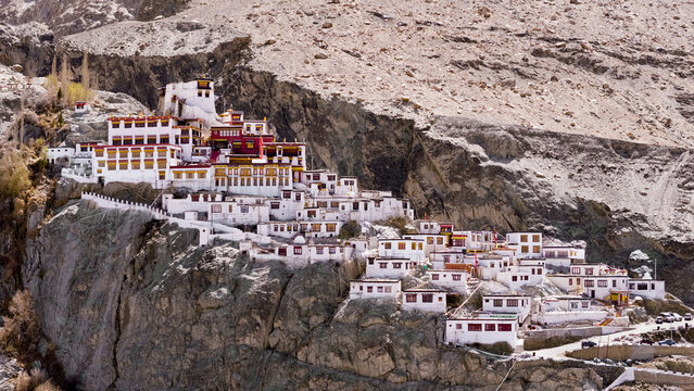 Aerial view of Diskit Monastery perched on a rocky cliffside with white buildings, red roofs, and rugged mountain terrain in Diskit, Ladakh, India.