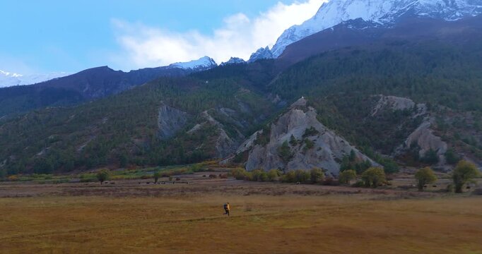 Annapurna Circuit, Manang, Nepal, aerial pull-out shot of a male hiker running along a trekking trail near Gangapurna Lake beneath snow-capped mountain peaks.
