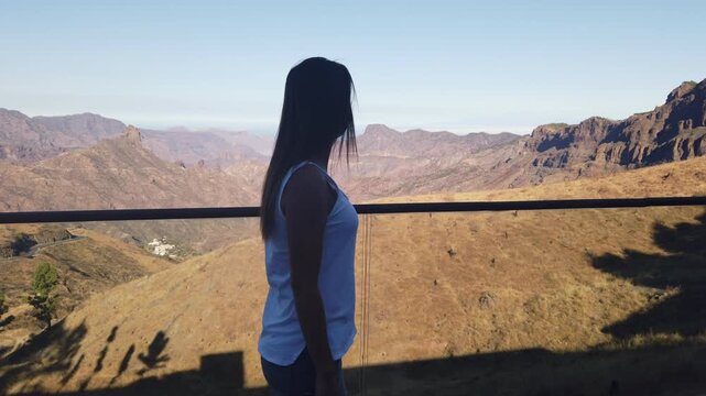 Woman standing on a balcony overlooking the stunning volcanic mountain landscape of Gran Canaria, enjoying the view of Roque Bentayga