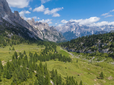 Aerial view of Rifugio Citta Di Carpi in the Dolomites, featuring lush alpine meadows, scattered pine trees, and rugged mountain peaks under a blue sky in Auronzo di Cadore, Veneto, Italy.