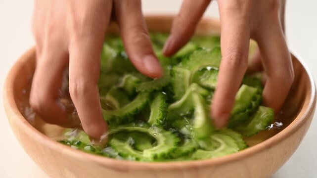 Woman hands mixing a sliced bitter gourd with salt and water in a wooden bowl to reduce bitterness