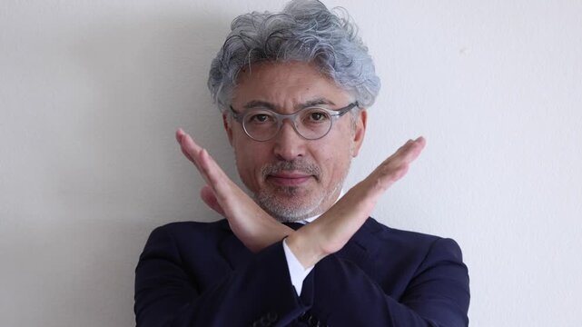腕でバツ印を作り拒否・禁止の意思を示すスーツ姿のシニア男性