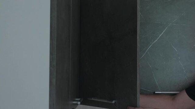 A handyman tightens fasteners with a screwdriver and checks the opening of a wall-mounted kitchen cabinet door. Professional furniture assembly and cabinet front adjustment during kitchen renovation.