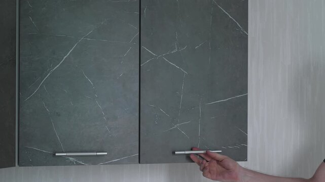 A handyman checking the alignment of a wall-mounted kitchen cabinet using a spirit level tool. Professional furniture assembly and installation quality control process at home.