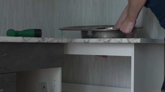 A professional handyman fits a round stainless steel sink into a marble countertop cutout. Home plumbing installation and modern kitchen furniture assembly process
