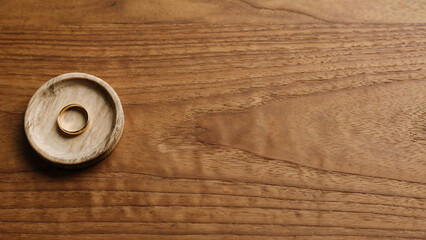 Fototapeta premium Minimalist gold wedding band on small wooden tray resting on timber table surface with ample copy space
