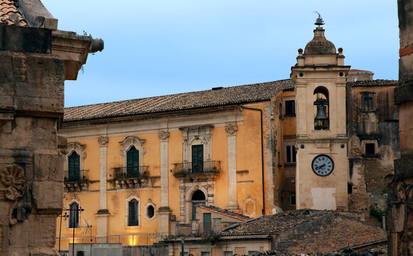 ancient European city square features a weathered town hall building with a classic clock tower and bell