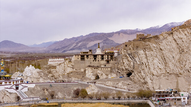 Aerial view of the historic Namgyal Tsemo Monastery perched on a rugged rocky cliff overlooking the town of Leh with snow-capped mountains in the background Leh, Ladakh, India.