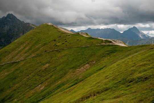 Hikers on a green mountain ridge under dramatic clouds