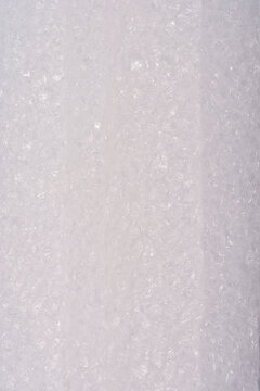 A detailed vertical close up view showing the cross section and porous texture of a white expanded plastic protective foam sheet used for packaging.
