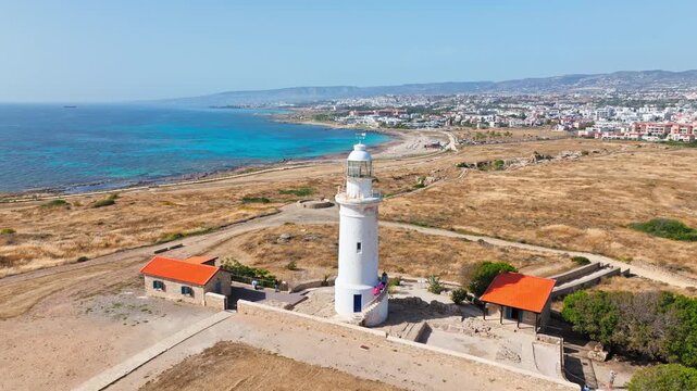 Aerial view of the lighthouse at Nea Paphos archaeological site in Cyprus. The white landmark, ancient grounds and Mediterranean Sea create a beautiful coastal heritage scene.