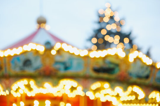 Abstract out of focus merry go round with glowing golden bokeh lights and a holiday pine tree.