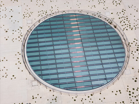 Aerial view of a large circular glass skylight with a metal frame set into a concrete plaza with small circular landscaping features in Kaunas, Kaunas County, Lithuania.