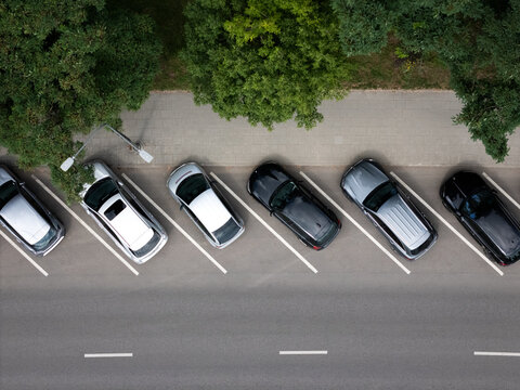Aerial view of cars parked in a row along a street with green trees and asphalt pavement in Kaunas, Kaunas County, Lithuania.