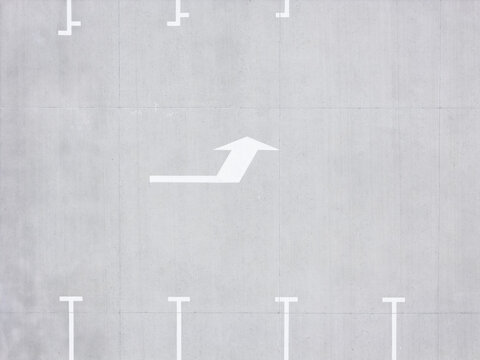 Aerial view of a parking lot with white painted directional arrows and parking space markings on grey asphalt in Kaunas, Kaunas County, Lithuania.