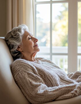 Mujer mayor descansando en un sill&oacute;n c&oacute;modo y manta suave. Rutina de descanso y confort