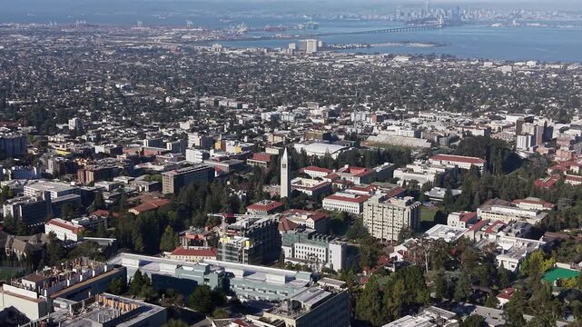 Aerial footage showcasing the University of California, Berkeley campus, with its notable Sather Tower, overlooking the sprawling cityscape and San Francisco Bay in the background. Push in drone shot