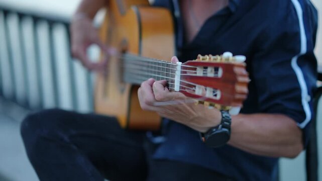 Street musician playing an acoustic classical guitar on a bench