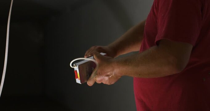 Electrician holds recessed LED light driver during ceiling installation indoors, twisting and tightening pieces before application