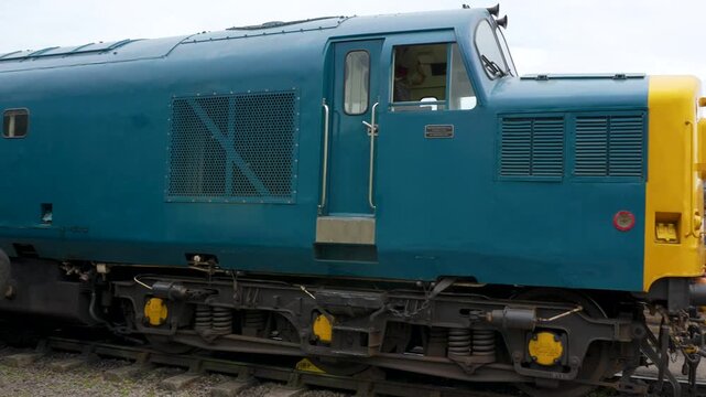 A closeup tracking shot showing the side profile and coupling mechanisms of classic British diesel locomotives at a train yard. Suitable for transport history and engineering documentaries.