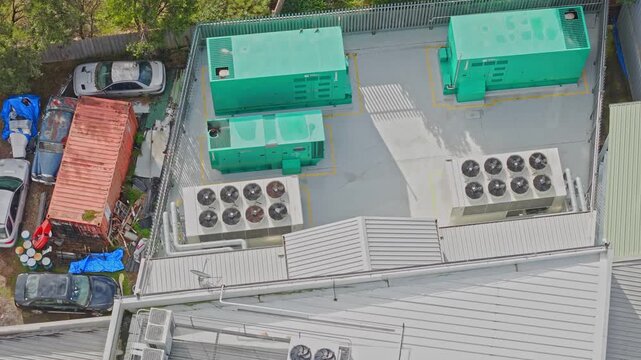 Drone shot of a secure data centre rooftop featuring industrial green generators, large HVAC units and fencing, under soft daylight. No people are visible, clean composition highlights facility.